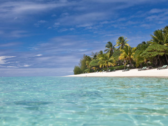 A beautiful image of sun-deck loungers set up in pairs on a long-stretched white sandy beach