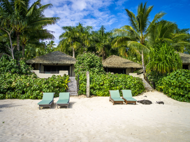 A thrilling image of two standalone Premium Beachfront Bungalows situated on the beach, with sundeck chairs set up in front of each Bungalow