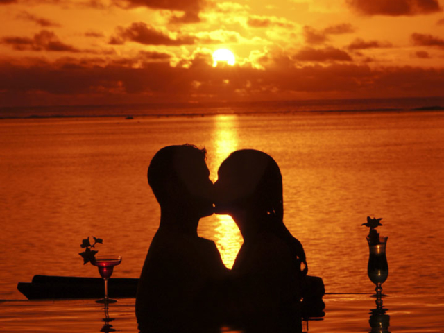 A couple enjoying sunset cocktails in the pool with a breath-taking sunset background