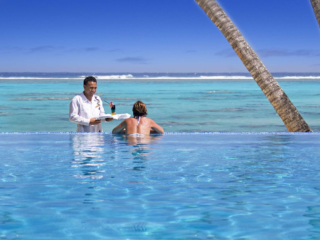 A woman accepting a cocktail from a waiter while admiring the beach views from the pool