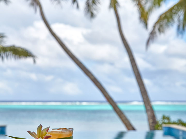 A flower garnished cocktail by the pool overlooking the beach