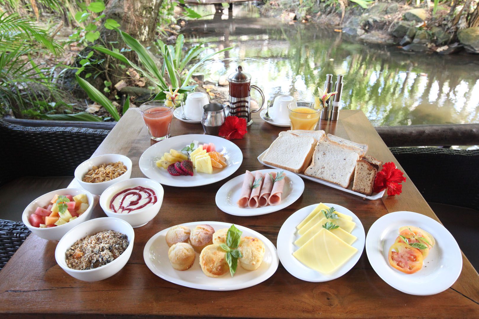 A delicious tropical continental breakfast selection set up featuring variety of breads, pastries, tropical fruits, ham and cheese along with a selection of coffee, tea and fruit juice