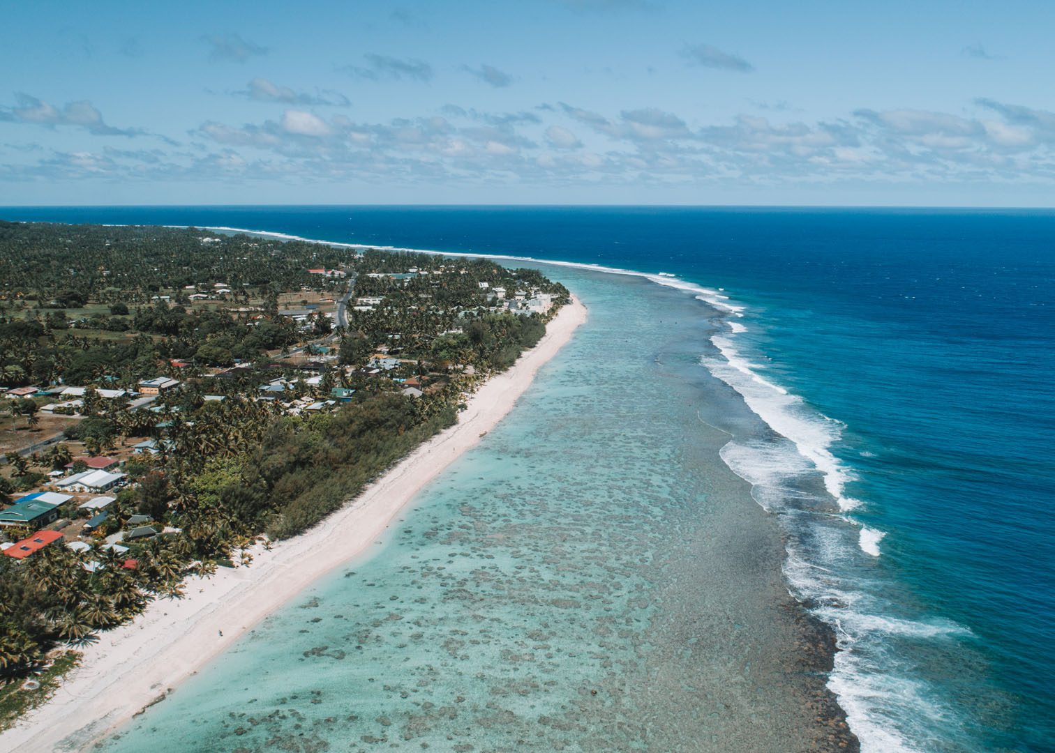 An aerial partial image of Rarotonga Island showing off the splashing of waves on the reef and the various blue shades of the Rarotonga waters