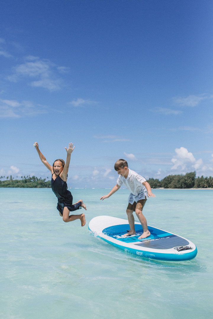 Young children pictured on the stand-up paddle board and jumping off to enjoy the warm waters of Rarotonga