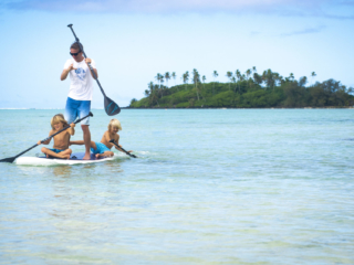 A beautiful image of father and two sons bonding in the lagoon sharing a stand-up paddleboard and smilingly paddles through the waters of Muri