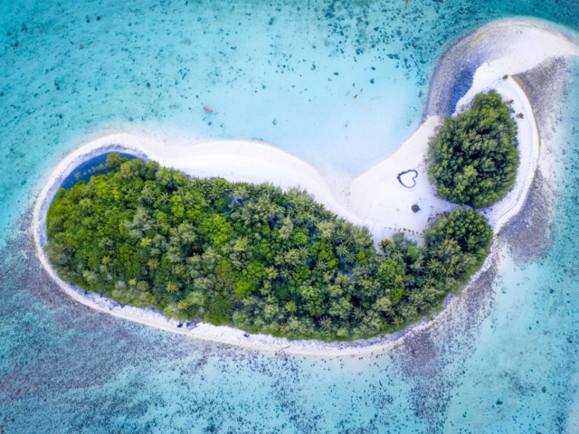 Aerial shot of Motu Koromiri amidst the Muri Blue Lagoon capturing a romantic heart-shaped sign printed on the white-sandy beach