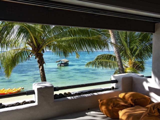 A close up view of the lagoon from the Premium Beachfront Suite private balcony, overlooking trimmed coconut palms that sway in the breeze on a tropical beach