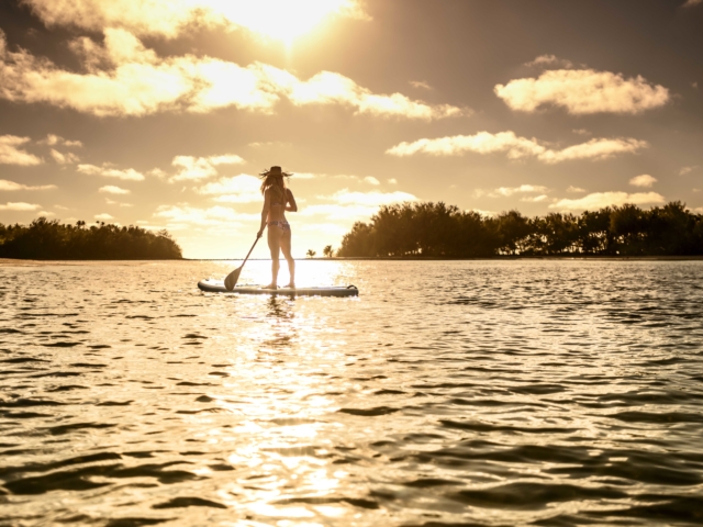 Resort guest stands on a floating paddle-board to greet the sunrise while admiring the scattering light across a greater region of the sky