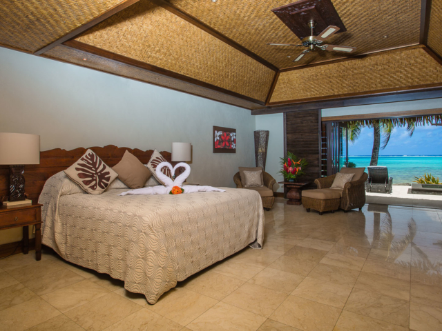 View of the Beachfront Villa Suite Interior with Polynesian inspired decor, with dark wooden trimmings and sliding doors opening out to the patio area overlooking the blue lagoon