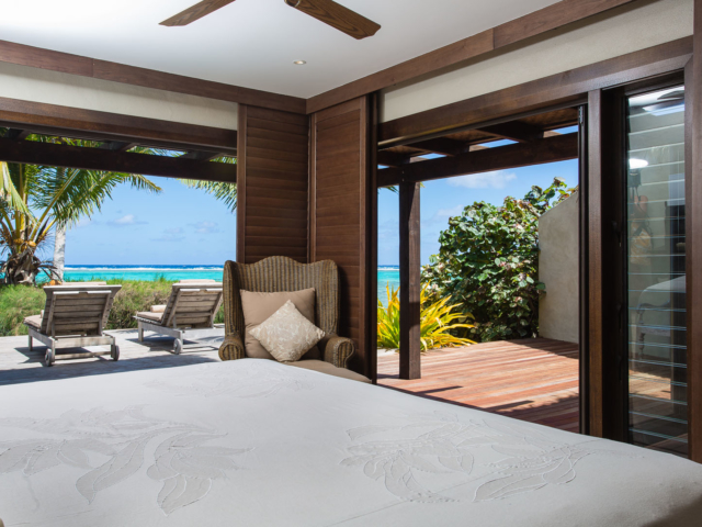 View from the second bedroom of the Presidential Beachfront Villa, with beautiful dark darkstained wooden trimmings with large siding doors leading out onto the deck over looking  a view of the lagoon