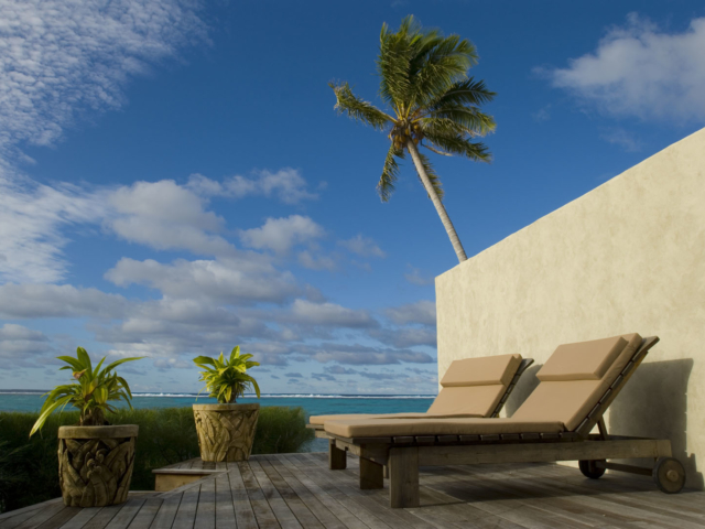 Loungers perfectly placed on the deck of the villa overlooking the lagoon with a swaying coconut tree in the background