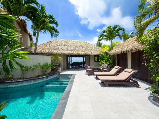 Ultimate beachfront villa courtyard beautifully set up with a view of the private pool, outdoor chairs and loungers offering an inviting feel on a stunning blue day