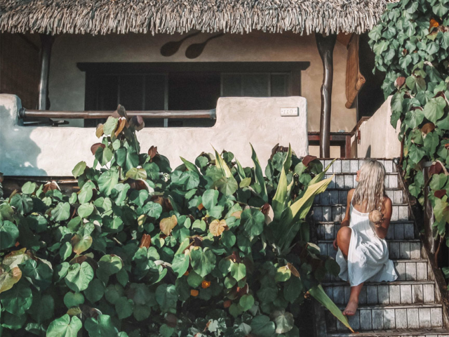 A lady sitting on the steps of the Premium Beachfront Bungalow, enjoying a coconut drink