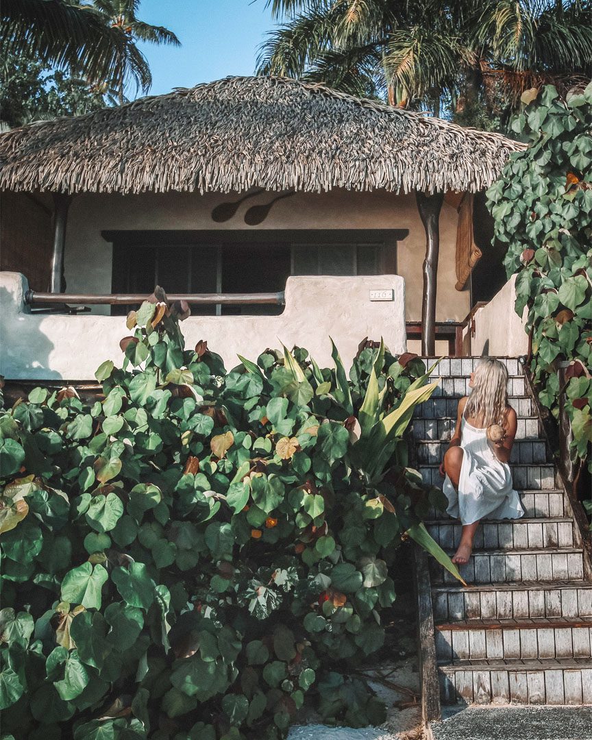A lady sitting on the steps of the Premium Beachfront Bungalow, enjoying a coconut drink