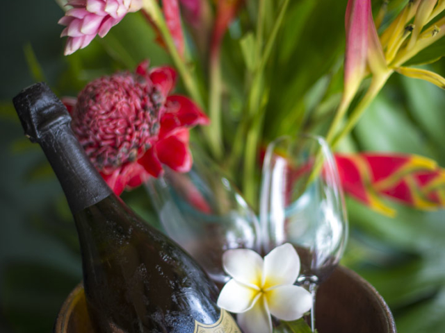 A chilled bottle of Champagne with flutes in a bucket of ice, set up next to a tropical floral arrangement