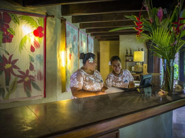 Guest Services Supervisor training a new front desk attendant at the reception desk, embedded with tropical flowers