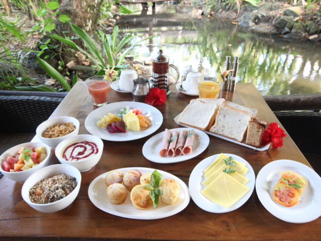 A delicious tropical continental breakfast selection set up featuring variety of breads, pastries, tropical fruits, ham and cheese along with a selection of coffee, tea and fruit juice