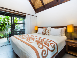Premium Family Room featuring a beautifully arranged king-sized bed in the midst of two Polynesian flares with a view of the garden in the back balcony