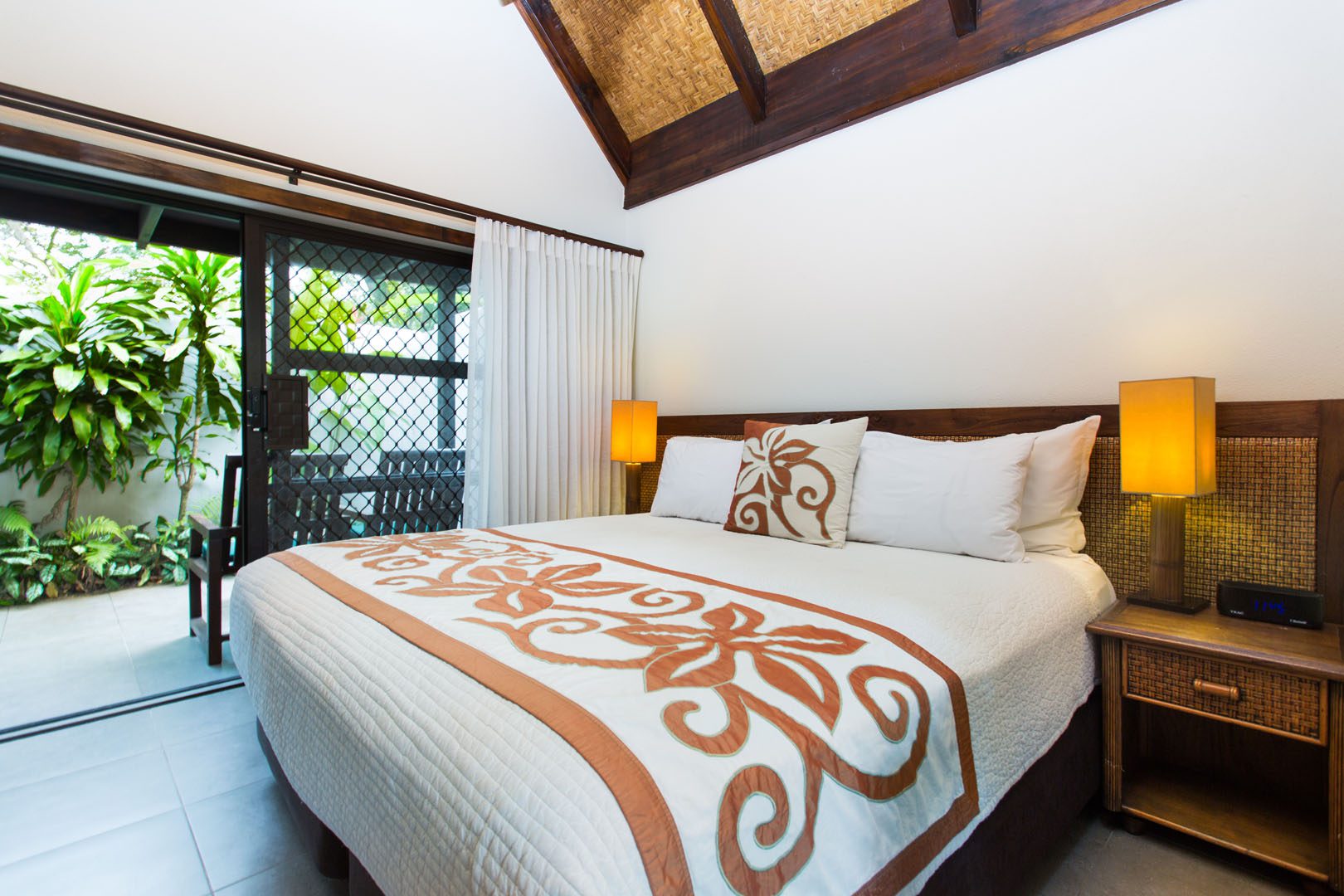 Premium Family Room featuring a beautifully arranged king-sized bed in the midst of two Polynesian flares with a view of the garden in the back balcony