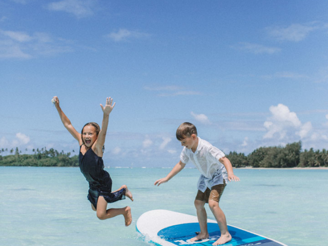 Young children pictured on the stand-up paddle board and jumping off to enjoy the warm waters of Rarotonga