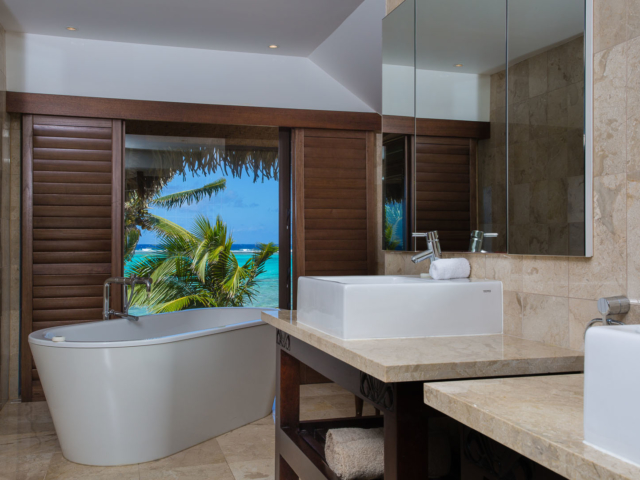 View of the modern Presidential Beachfront Villa Bathroom, with a large bath overlooking a view of the blue lagoon