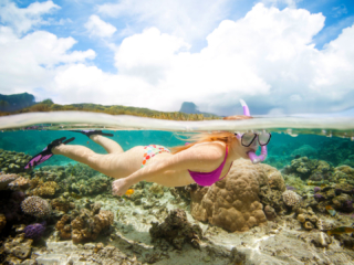 Snorkelling in the clear blue lagoon on a sunny day with Te manava in the background