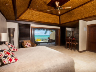 Inside view of the Villa Suite Bedroom, with Polynesian decor, dark wooden trimmings leading onto sliding doors the showcase a view of the beautiful lagoon
