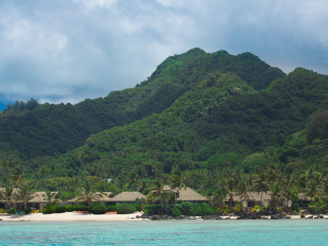 View of Te Manava Luxury Villas and Spa from the lagoon with green lush tropical trees and mountains