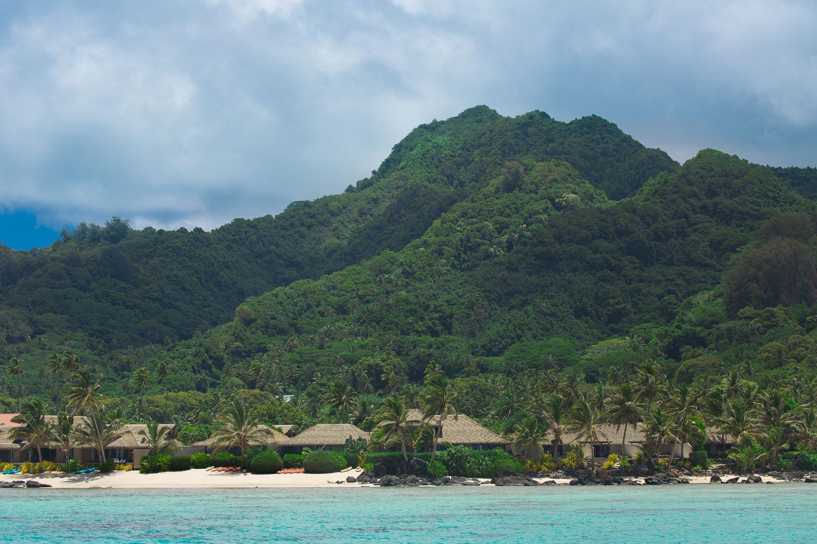 View of Te Manava Luxury Villas and Spa from the lagoon with green lush tropical trees and mountains