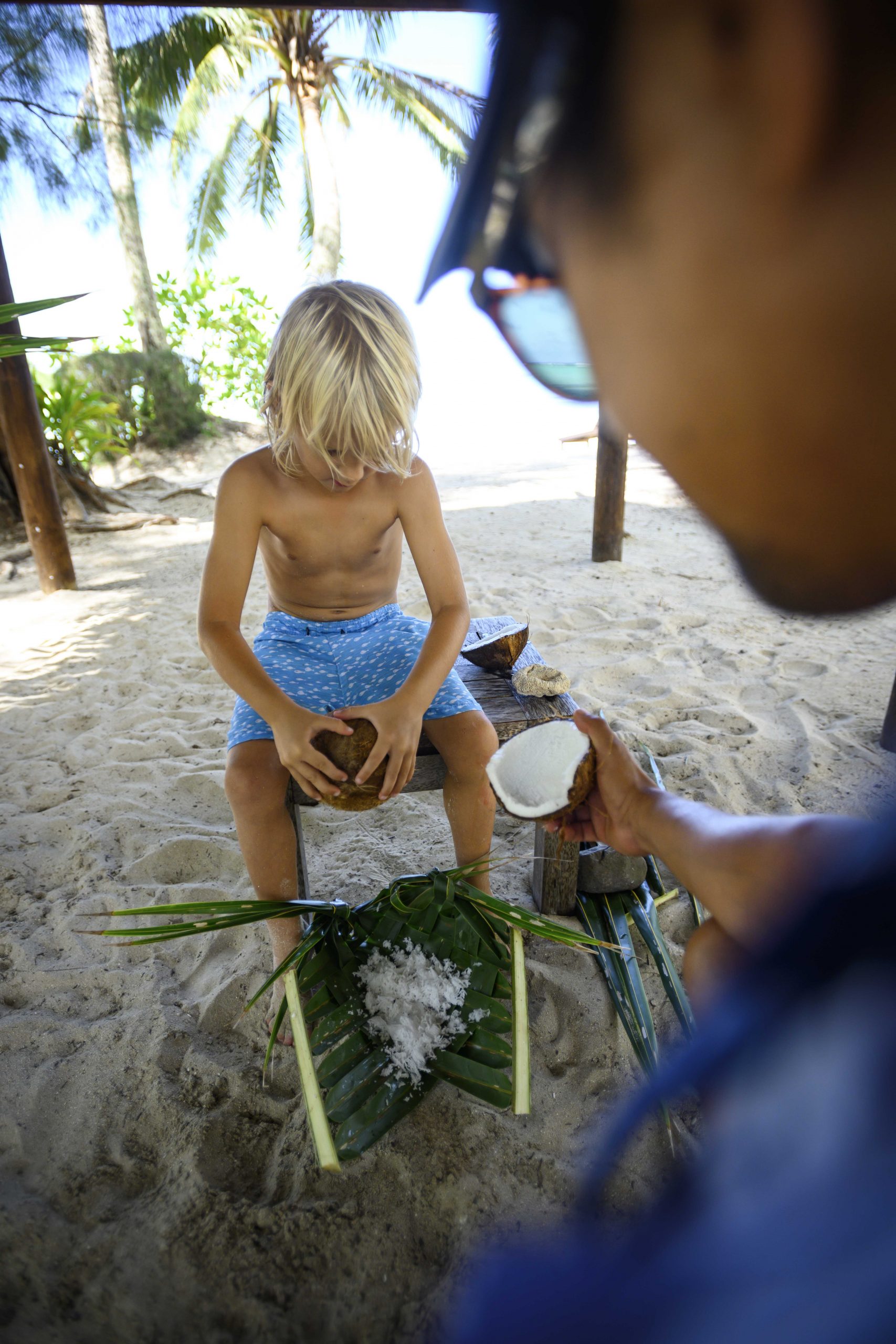 Supervised coconut grating by the beach, performed by a young boy with the help of the Resort Attendant