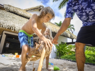 A supervised coconut husking performed by a young boy with the help of the Resort Attendant
