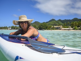 A Resort guest works on her sun tan leaning towards the stand-up paddleboard with both hands resting on the board while her hip and legs submerged into the warm waters of the Muri Lagoon