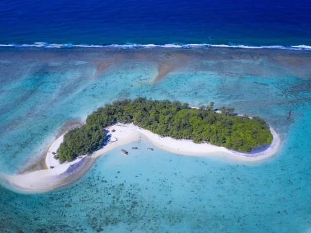 A spectacular aerial image of Motu Koromiri, a secluded private island set amidst the clear blue lagoon showcasing the splashing of waves towards the outer reef