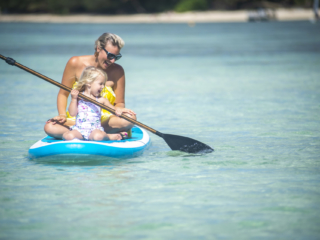 Image of mum enjoy coaching daughter, a toddler, the paddle moves on the paddle-board along the Muri Lagoon
