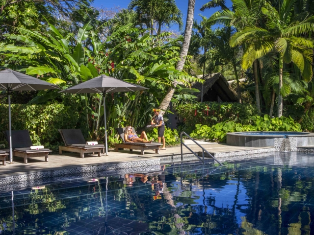 Resort guest relaxes on a sun lounge by the swimming pool, situated amidst the tropical lush garden for more privacy