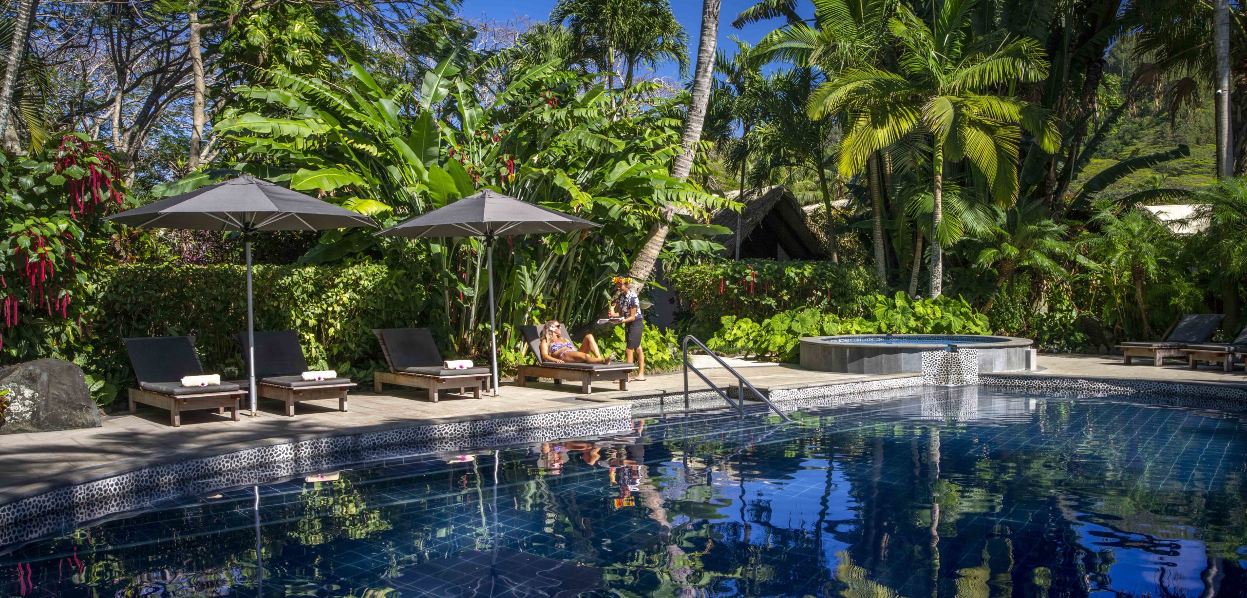 Resort guest relaxes on a sun lounge by the swimming pool, situated amidst the tropical lush garden for more privacy