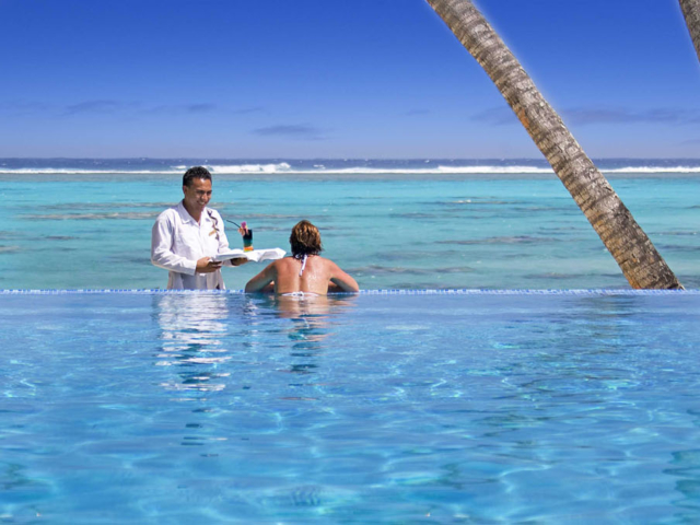 A woman accepting a cocktail from a waiter while admiring the beach views from the pool