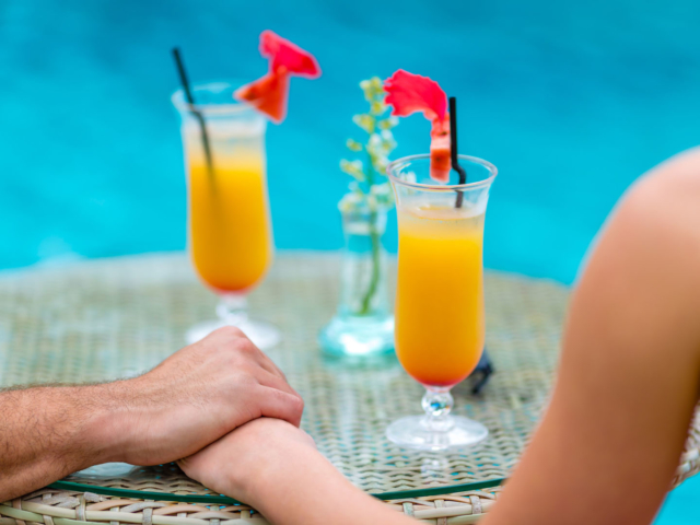 A couple holding hands enjoying cocktails by the pool
